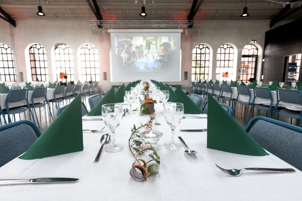 Långbord med festligt dukade bord. Stora fönster och projektor längs väggen.